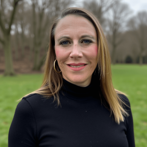 Sarah Merritt Ryan wearing a black sweater and standing outside in front of woods